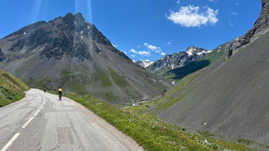 Cyclists on an empty mountain road winding through a valley below a rocky peak