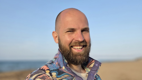 Danny smiling on a sunny beach, wearing a colorful patterned jacket